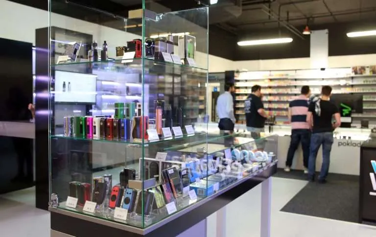 Lit acrylic and glass retail counter cases displaying vape and e-cigarette products in a shop