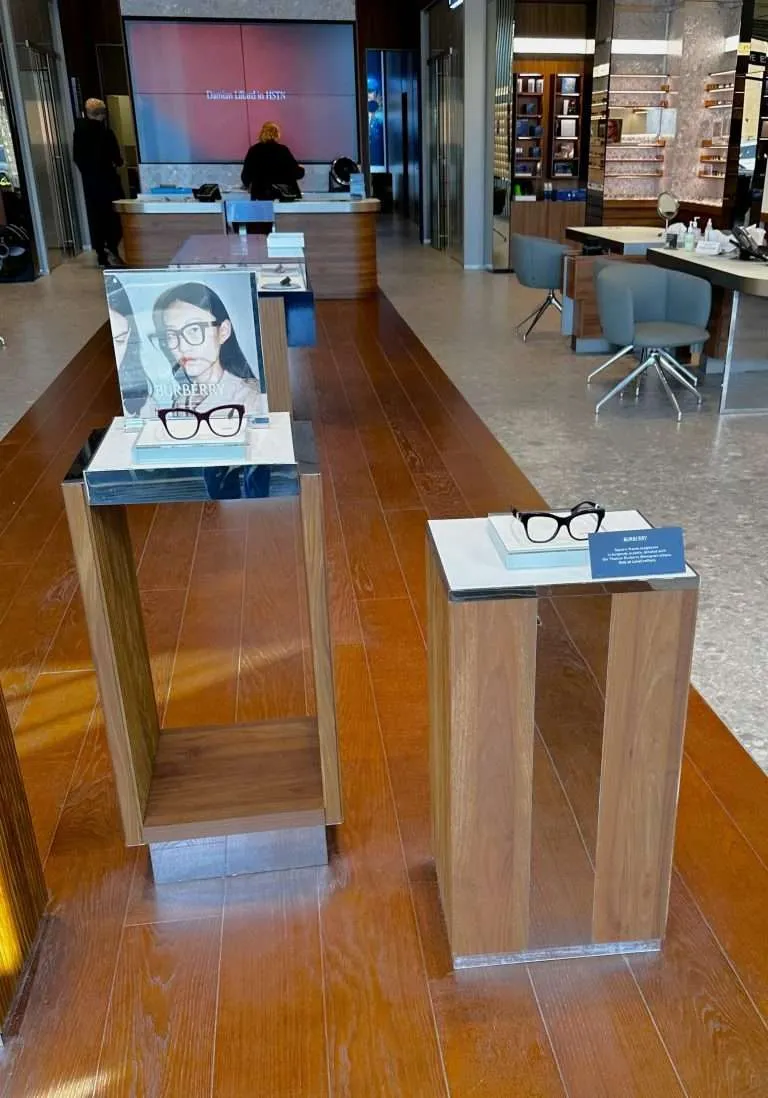 Eyewear display pedestals combining natural wood, clear acrylic, and mirrored acrylic panels