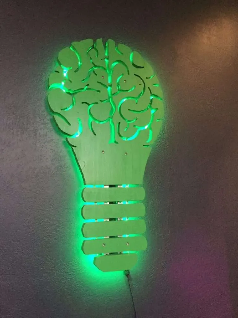 Wall-mounted lightbulb-and-brain sign with green LED backlighting.