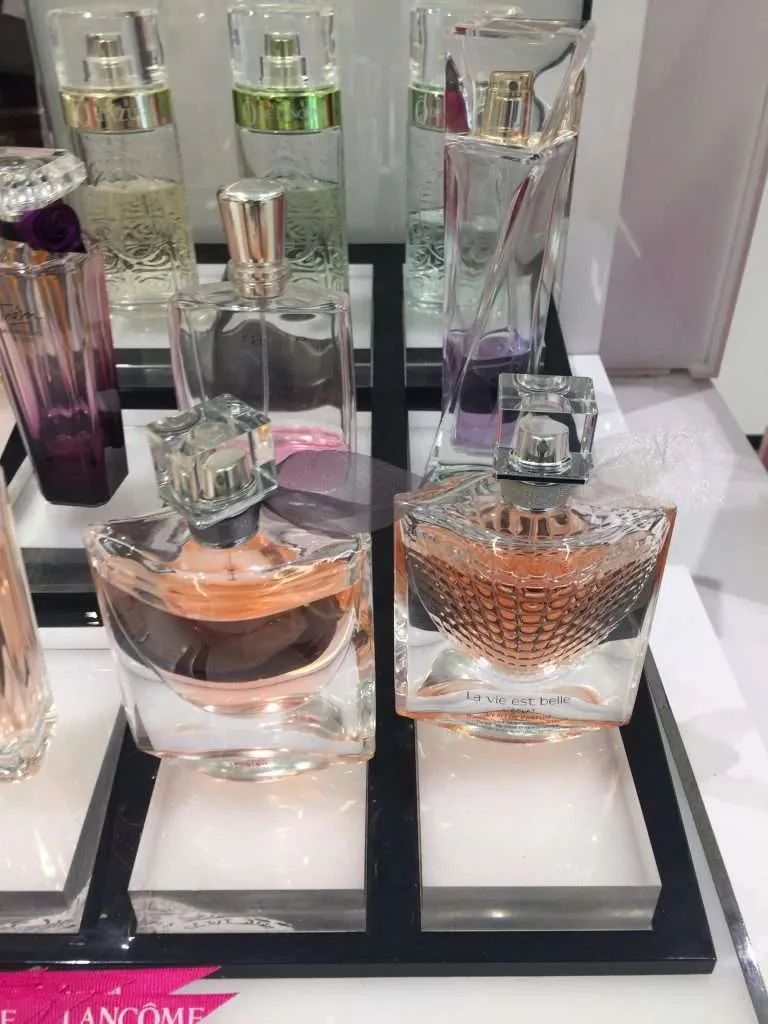 Black acrylic riser trays displaying perfume bottles at a cosmetics counter.