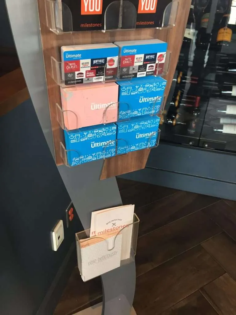 Wall-mounted clear acrylic holder displaying gift cards and a brochure pocket.