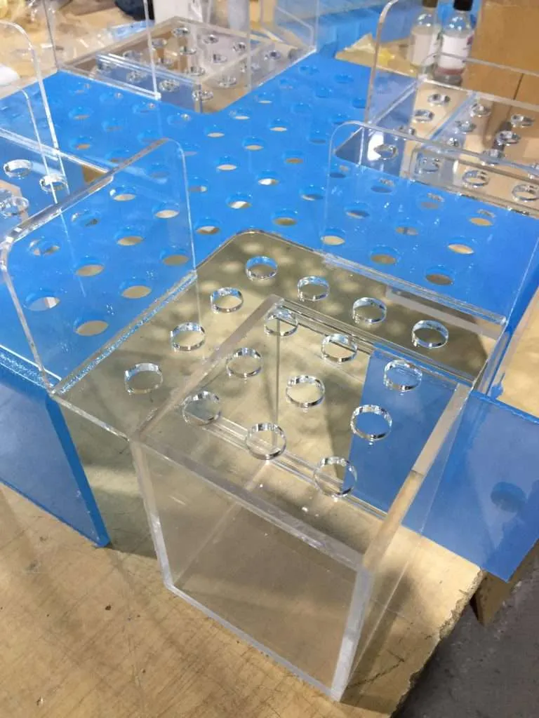 Clear and blue-tinted acrylic laboratory containment enclosures with ventilation holes.