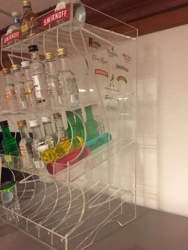 Clear acrylic cabinet with white shelves holding miniature spirit bottles and printed logos