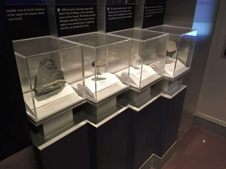 Row of clear acrylic display cases protecting mineral specimens with interpretive labels in a museum.