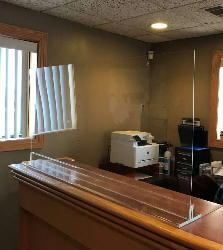 Clear acrylic protective shield mounted on a wood reception desk