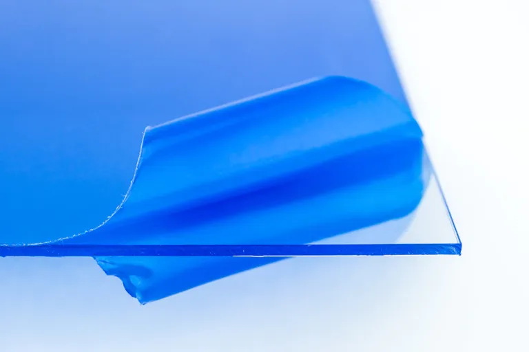 Corner of a clear acrylic sheet with blue protective masking film peeling back.