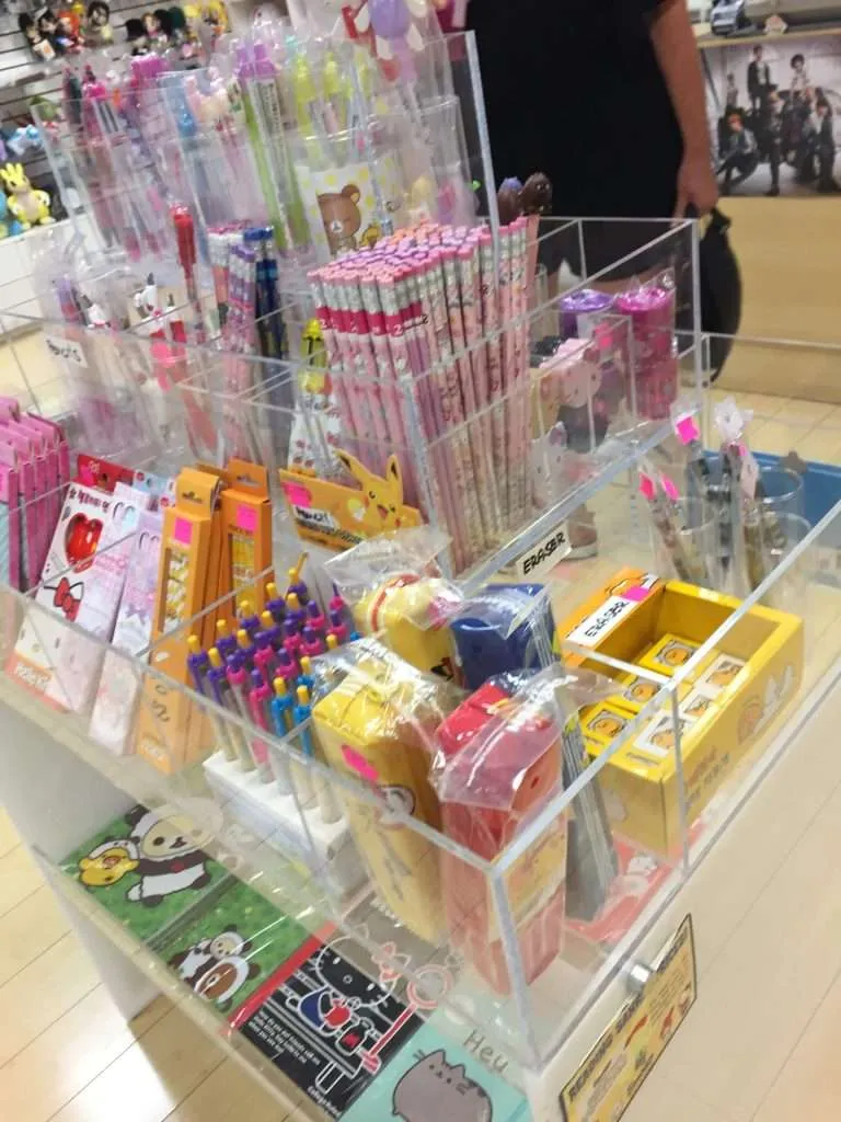 Clear acrylic three-tier bin display with divided compartments holding stationery in a shop