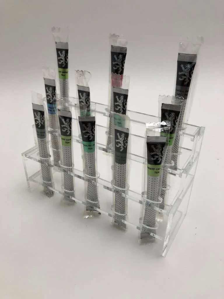 Clear acrylic tiered dispenser holding individually wrapped beverage sticks in slots.