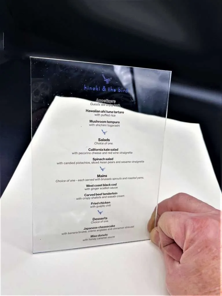 Clear acrylic restaurant menu with full-color printed text held in a hand