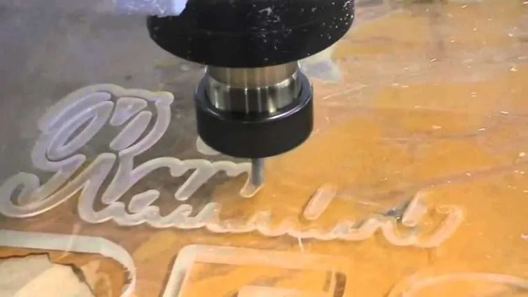A CNC router carving cursive letters from clear acrylic sheet.