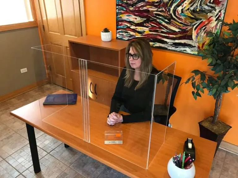 Freestanding clear acrylic desk shield with a pass-through on an office desk