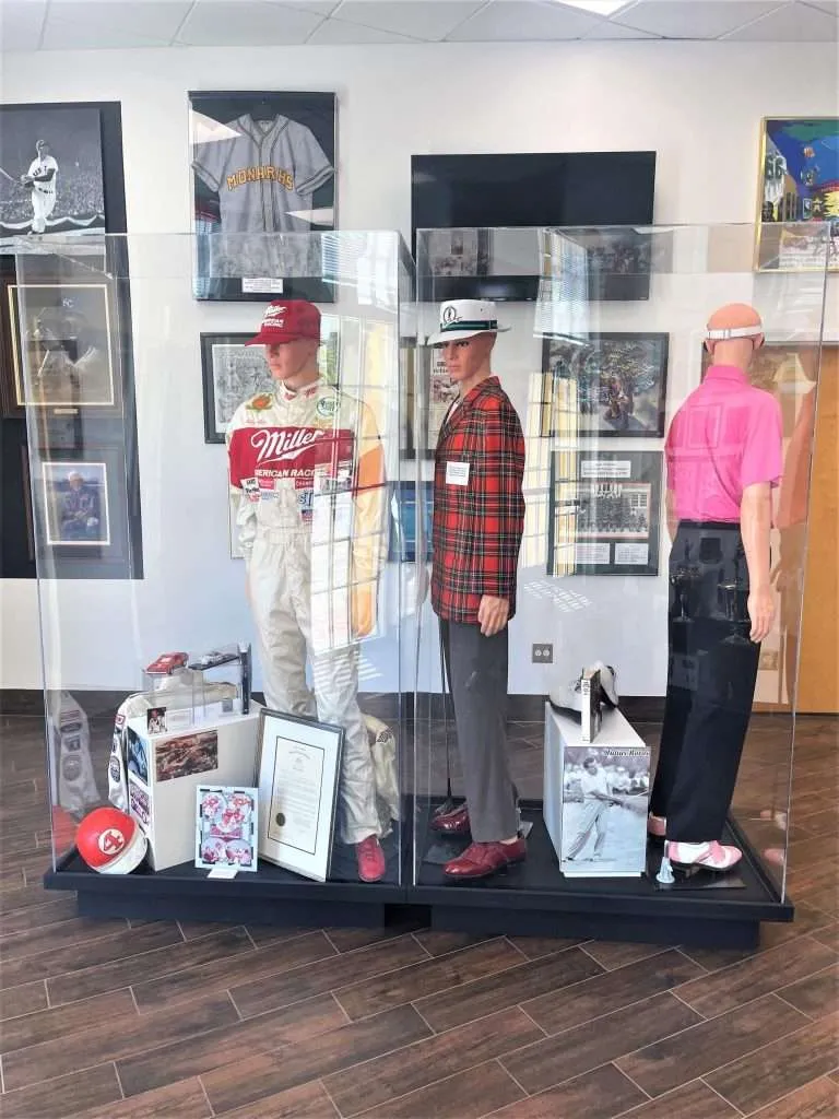 Full-height clear acrylic display case housing sports uniforms and memorabilia