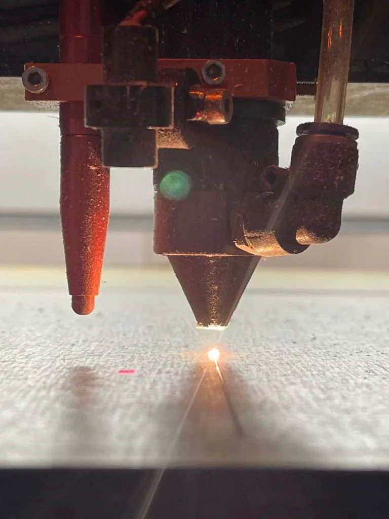 Close-up of a laser cutter head cutting a sheet of material with a bright cutting point