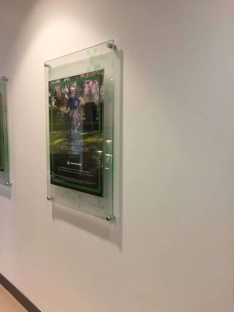 Wall-mounted clear acrylic poster frame held by metal standoffs.